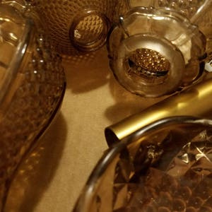 May include: An assortment of vintage amber glass bottles and decorative pieces. The bottles have various textures, including diamond and bubble patterns. The warm amber color and intricate designs suggest a collection of antique or retro glassware.