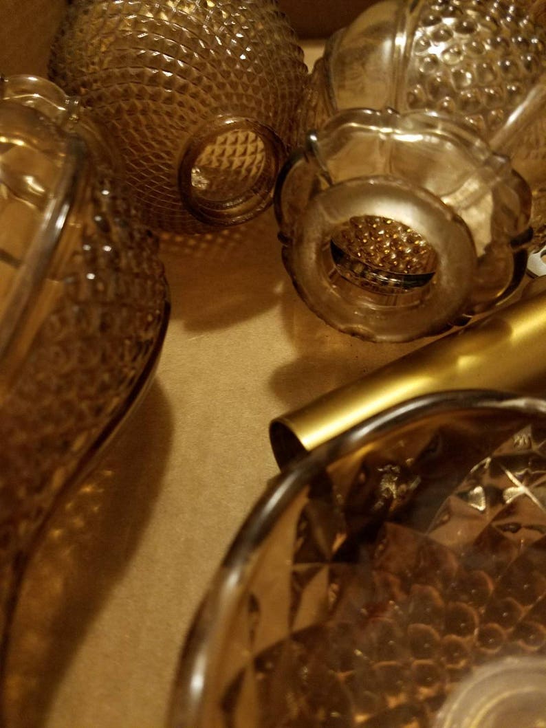 May include: An assortment of vintage amber glass bottles and decorative pieces. The bottles have various textures, including diamond and bubble patterns. The warm amber color and intricate designs suggest a collection of antique or retro glassware.