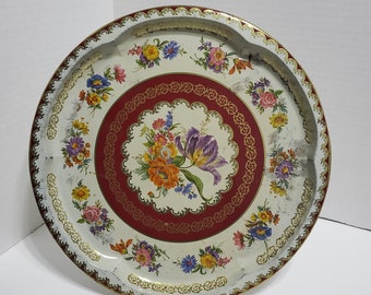 May include: A vintage metal serving tray with a white background and a red border. The tray is decorated with a floral pattern in shades of red, yellow, purple, and green. The tray has a gold rim and a gold floral design around the edge.