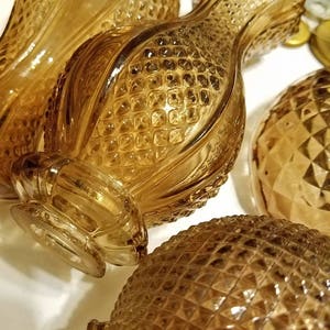 May include: Close-up of several amber-colored glass vases with textured, diamond-shaped patterns. The vases have a pineapple-like design, with a bulbous body and a flared neck. The glass reflects light, creating highlights and shadows.