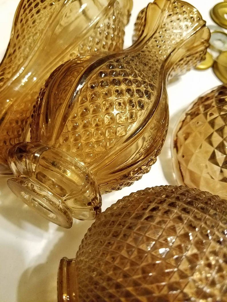 May include: Close-up of several amber-colored glass vases with textured, diamond-shaped patterns. The vases have a pineapple-like design, with a bulbous body and a flared neck. The glass reflects light, creating highlights and shadows.