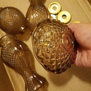 May include: Several vintage amber glass perfume bottles and atomizer tops. The bottles have a diamond pattern and a bulbous shape. The atomizer tops are gold-colored. The bottles are in a cardboard box.