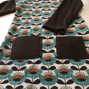 May include: A brown and teal long-sleeved dress with a floral pattern. The dress has two large pockets on the front.