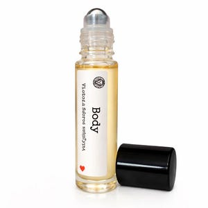 May include: A clear glass roll-on bottle with a silver rollerball top and a black cap. The bottle contains a light yellow liquid and has a white label with the word "Body" and other text. A red heart is at the bottom.