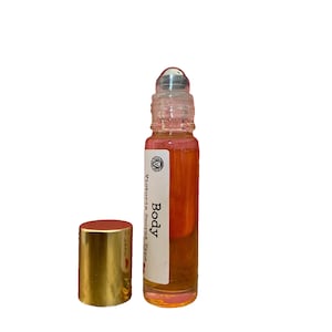 May include: A clear glass roll-on bottle with a gold cap. The bottle is filled with a light orange liquid. The label on the bottle reads "Victoria Secret Type Body".