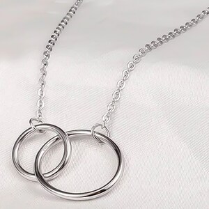 May include: A silver necklace with two interlocking circles as a pendant. The chain is a delicate, linked style.