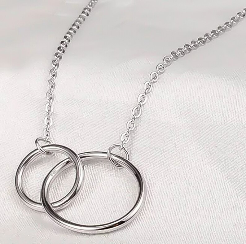May include: A silver necklace with two interlocking circles as a pendant. The chain is a delicate, linked style.