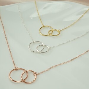May include: Three delicate necklaces with interlocking circle pendants. The necklaces are silver, gold, and rose gold.