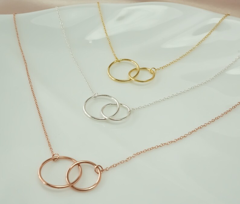 May include: Three delicate necklaces with interlocking circle pendants. The necklaces are silver, gold, and rose gold.