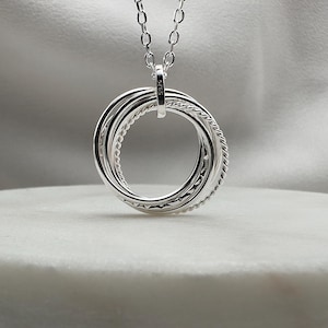 May include: Silver necklace with a pendant featuring five interlocking rings. The pendant is marked with the number "925", indicating it is made of sterling silver.