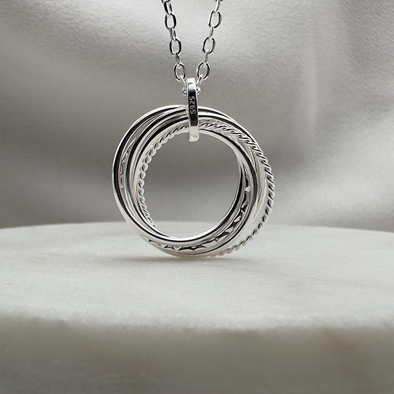 May include: Silver necklace with a pendant featuring five interlocking rings. The pendant is marked with the number "925", indicating it is made of sterling silver.