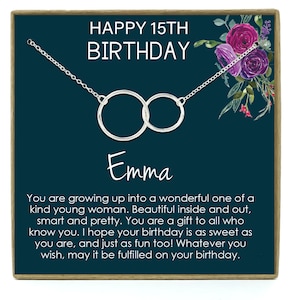 May include: A teal blue gift box with a silver necklace featuring two interlocking circles. The box has a floral design with pink and purple flowers. The text "HAPPY 15TH BIRTHDAY" is printed in white at the top of the box. The name "Emma" is written in cursive below the necklace. The text "You are growing up into a wonderful one of a kind young woman. Beautiful inside and out, smart and pretty. You are a gift to all who know you. I hope your birthday is as sweet as you are, and just as fun too! Whatever you wish, may it be fulfilled on your birthday." is printed below the name.