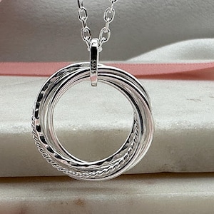 May include: A silver necklace with a pendant made of five interlocking rings. The rings are twisted and have a textured surface.
