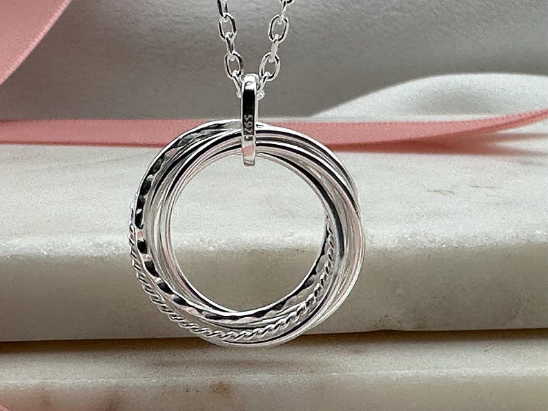 May include: A silver necklace with a pendant made of five interlocking rings. The rings are twisted and have a textured surface.
