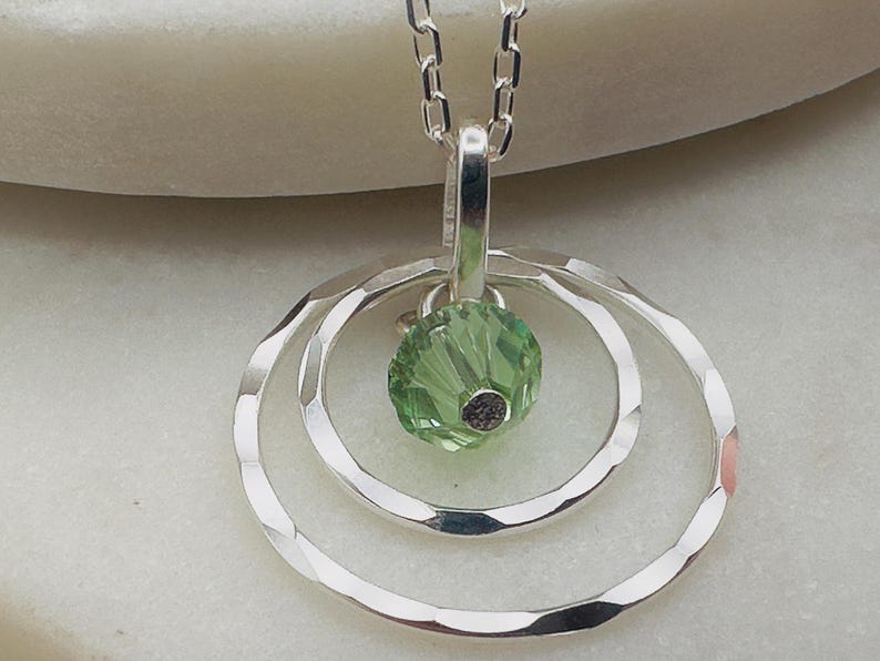 May include: A silver necklace with a pendant featuring three concentric circles and a green crystal in the centre.