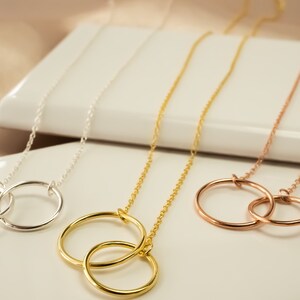 May include: Three gold necklaces with interlocking circle pendants. The necklaces are silver, gold, and rose gold.