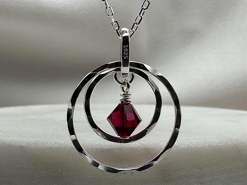 May include: A silver necklace with a pendant featuring two interlocking circles and a dark red crystal. The pendant is marked with "S925".