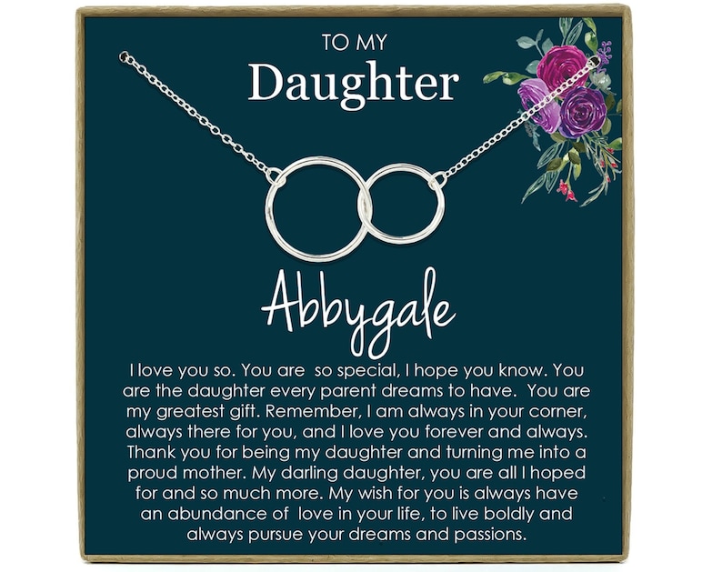 May include: A teal blue card with a silver necklace featuring two interlocking circles. The card has the text "To My Daughter Abbygale" and a message about love and support.