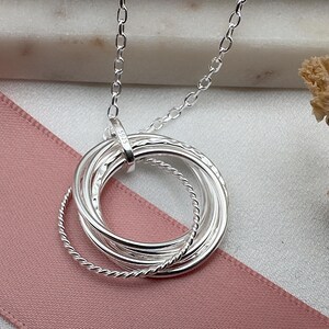 May include: Silver necklace with a pendant made of five interlocking rings. The rings are textured and have a polished finish. The necklace is 925 silver.