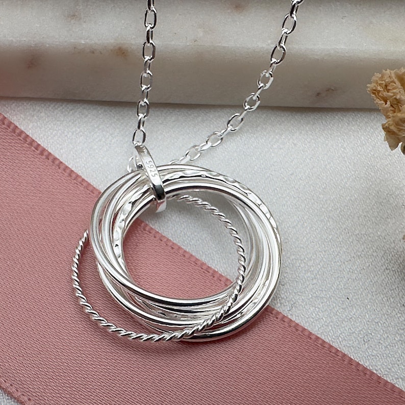 May include: Silver necklace with a pendant made of five interlocking rings. The rings are textured and have a polished finish. The necklace is 925 silver.