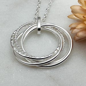 May include: Silver necklace with a pendant featuring four interlocking circles. The circles are textured and have a polished finish.