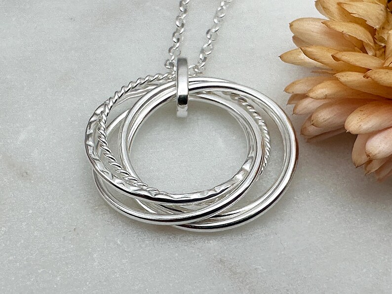 May include: Silver necklace with a pendant featuring four interlocking circles. The circles are textured and have a polished finish.