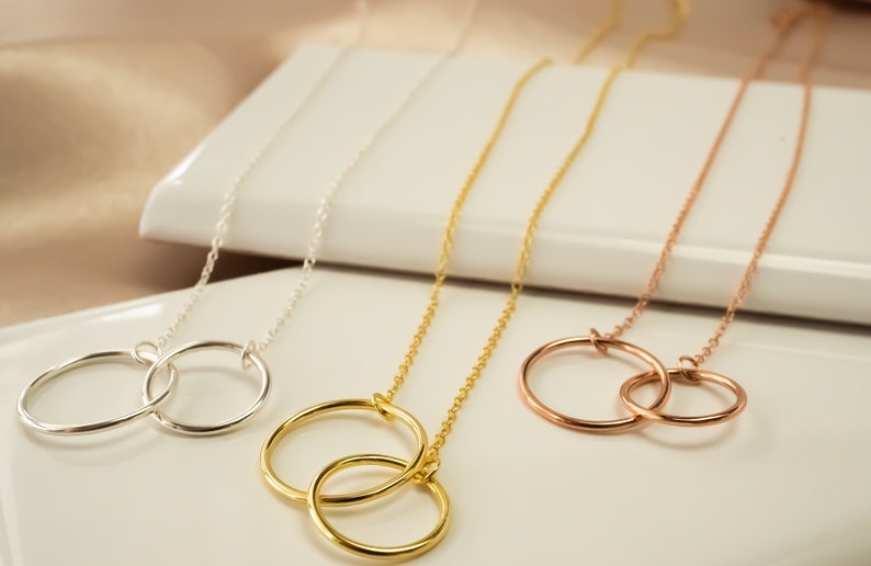 May include: Three gold necklaces with interlocking circle pendants. The necklaces are silver, gold, and rose gold.