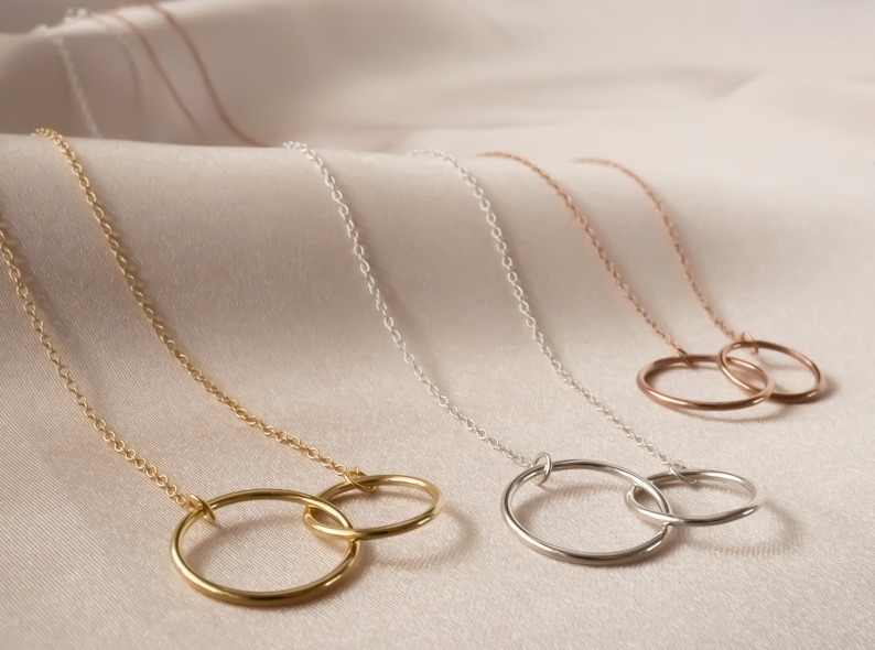May include: Three gold necklaces with interlocking circle pendants. The necklaces are in gold, silver, and rose gold.
