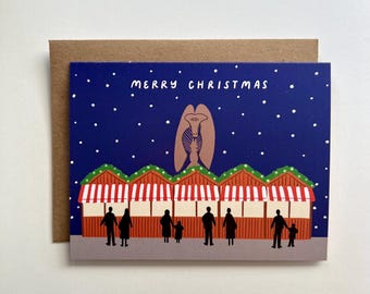 May include: A Christmas card with a blue background and white snowflakes. The card features a red and white striped market stall with people standing in front of it. The text "Merry Christmas" is at the top of the card.