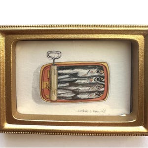 May include: A framed watercolor painting of a sardine can. The can is open, revealing several fish. The frame is gold-colored and rectangular. The painting is signed "Valerie C. Haniell".