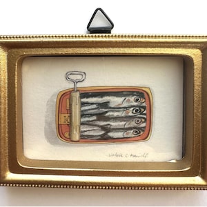 May include: A framed watercolor painting of a sardine can. The can is open, revealing several fish. The frame is gold-colored, and the painting is signed by the artist. The painting is a still life.