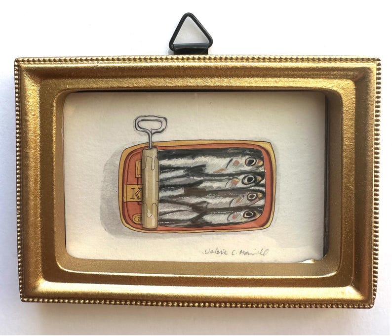 May include: A framed watercolor painting of a sardine can. The can is open, revealing several fish. The frame is gold-colored, and the painting is signed by the artist. The painting is a still life.