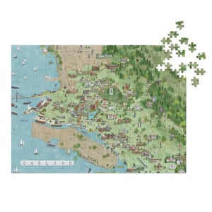 Könnte beinhalten: Ein farbenfrohes Puzzle, das eine Karte von Oakland, Kalifornien, zeigt, mit dem Wort "OAKLAND" sichtbar. Das Puzzle zeigt Illustrationen von Gebäuden, Bäumen und Booten, mit einigen separaten Teilen.