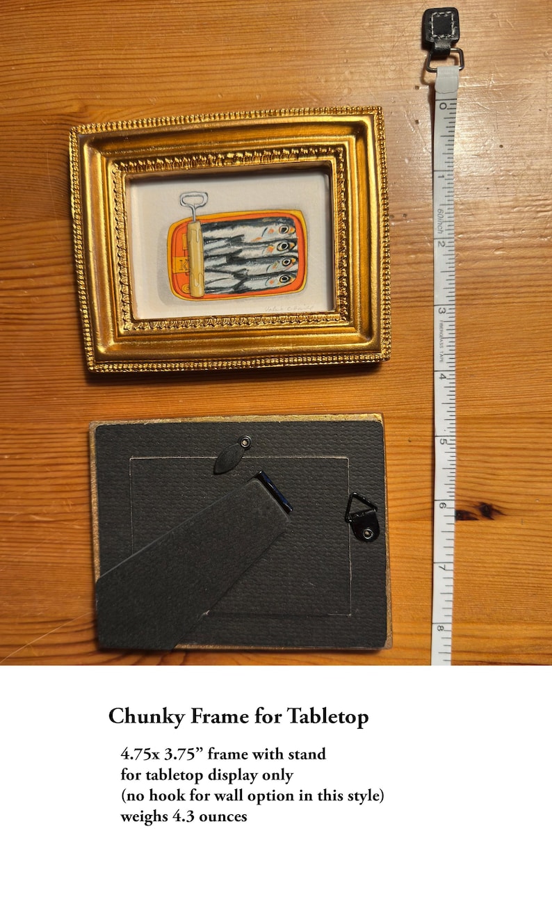 May include: A gold-colored, ornate picture frame with a small painting of sardines in a can. The frame is 4.75 inches by 3.75 inches and includes a stand for tabletop display. The frame weighs 4.3 ounces.