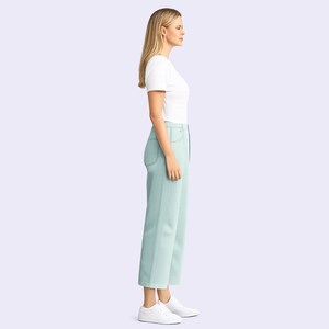 Puede incluir: Una camiseta blanca de manga corta con cuello redondo combinada con pantalones de talle alto en color verde menta claro con costuras visibles en los bolsillos y laterales, junto a zapatillas blancas sobre un fondo claro.