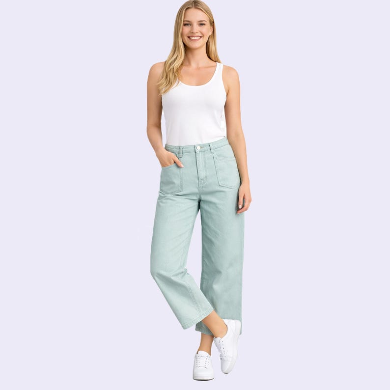 Puede incluir: Una camiseta sin mangas blanca combinada con pantalones de pierna ancha y cintura alta en color verde salvia claro, con dos grandes bolsillos delanteros, cierre de bot&oacute;n y cremallera, y zapatillas blancas, creando un conjunto casual.