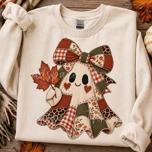 Op de afbeelding: Een crèmekleurige sweater met ronde hals en een centrale afbeelding van een geest gemaakt van diverse patchworkpatronen, waaronder rood ruitjespatroon, groene corduroy, luipaardprint en bloemmotieven. De geest draagt een grote strik.
