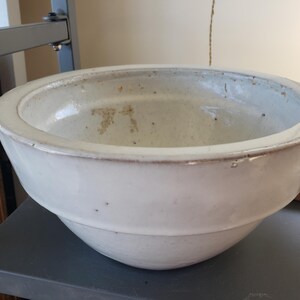Peut inclure: Un bol mélangeur rond en céramique blanc cassé avec un bord large et plat et un design extérieur étagé. La surface intérieure présente des signes d'usure avec des taches brun clair visibles et de petites taches sombres sur la finition émaillée.