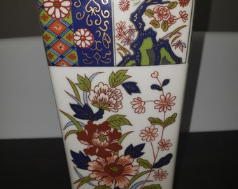 May include: A white ceramic vase with a square base and a floral design. The vase is decorated with red, blue, green, and gold flowers and leaves. The vase has a traditional Japanese style.
