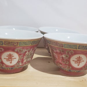 May include: Set of four red and white porcelain bowls with a gold trim and Chinese characters. The bowls have a floral design and a raised pattern.
