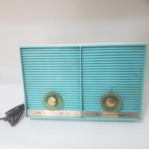 May include: A vintage turquoise Philco twin speaker radio with gold detailing. The radio has a horizontal ribbed design, two gold knobs labelled "Volume" and "twin speaker", and a black power cable.