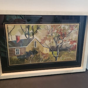 Peut inclure: Peinture à l'aquarelle encadrée d'une maison jaune avec un toit rouge et un arbre aux feuilles rouges. La peinture est signée "Ella Briejeson".