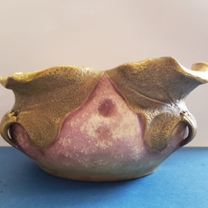 May include: A ceramic bowl with a pink and gold glaze. The bowl has a unique, organic shape with leaf-like details.