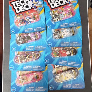 May include: Eight Tech Deck fingerboards in original blister packaging featuring Sonic the Hedgehog characters. Each skateboard displays unique graphics of Sonic, Shadow, Knuckles, Amy, and Chao on the deck, with metal trucks and white wheels.