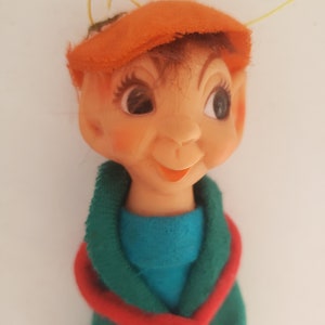 Peut inclure: Une poupée d'elfe vintage vêtue d'une tenue verte et rouge, d'un chapeau orange et de cheveux bruns. La poupée a de grands yeux bruns et un visage souriant.