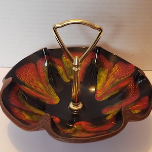 May include: A black ceramic serving dish with a gold handle. The dish has a scalloped edge and is decorated with swirls of red, orange, and yellow.