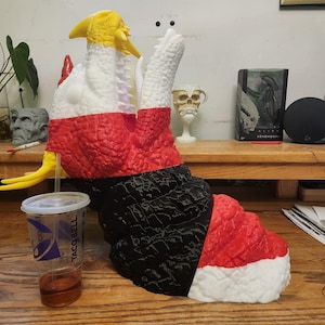 May include: A large, textured sculpture of a monster in red, black, white, and yellow. The monster has a long neck and a wide open mouth. A clear plastic cup with a Taco Bell logo is in front of the sculpture.