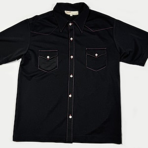 May include: A black short-sleeved button-down shirt with a red stitching detail around the collar and pockets. The shirt has a pointed collar and two chest pockets.