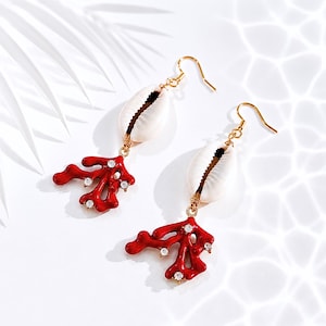 Peut inclure: Une paire de boucles d'oreilles dorées avec des pendentifs en coquillage blanc et des breloques en forme de corail rouge vif. Les breloques en corail sont ornées de petits cristaux étincelants. Les boucles d'oreilles ont une fermeture à crochet.