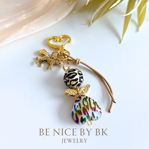 May include: A gold-tone keychain with a leopard print charm, a small gold-tone animal charm, and a heart-shaped charm with a leopard print design. The keychain is attached to a brown leather cord.